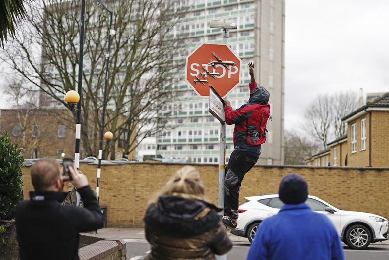 Una persona retira una obra de arte de Banksy que parece mostrar tres drones sobre un cartel de Stop que fue develado en la intersección de las calles Southampton Way y Commercial Way en Peckham, sureste de Londres, viernes 22 de diciembre de 2023. (Aaron Chown/PA via AP)