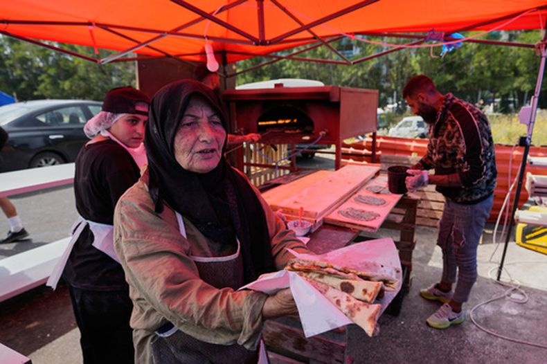 Soubhiye Zeiter, de 63 años, una mujer desplazada que huyó de su hogar con su familia en los suburbios del sur de Beirut debido a la guerra entre Israel y Hezbollah, distribuye manaeesh, un popular desayuno libanés de pan plano cubierto con tomillo en una pequeña panadería de un asentamiento con tiendas de campaña junto al paseo marítimo de Beirut, Líbano, jueves 21 de mayo de 2026. (Foto AP/Hussein Malla)