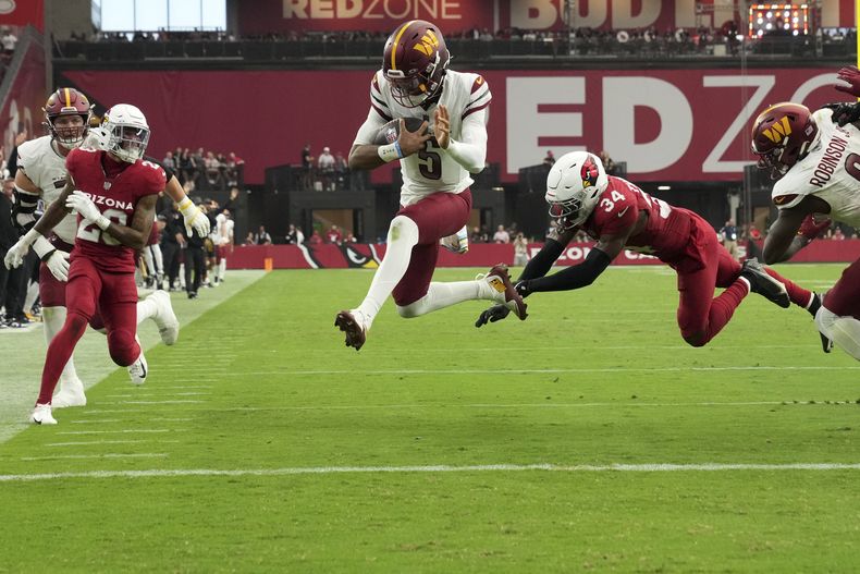 El quarterback de los Commanders de Washington, Jayden Daniels (5), salta a la zona de anotación para un touchdown mientras el safety de los Cardinals de Arizona, Jalen Thompson (34), defiende durante la segunda mitad de un partido, el domingo 29 de septiembre de 2024, en Glendale, Arizona (AP Foto/Rick Scuteri)