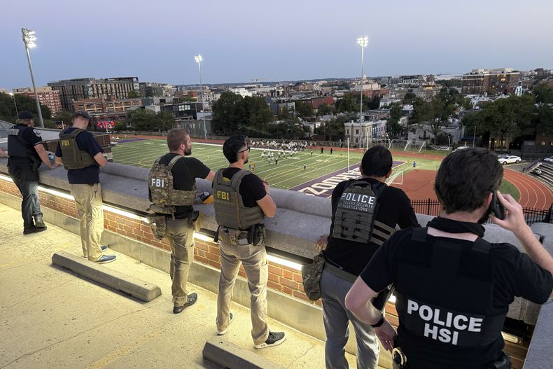 Agentes del Departamento de Policía Metropolitana, del FBI y de Investigaciones de Seguridad Nacional (HIS, por sus siglas en inglés), vigilan un juego de fútbol americano entre Bell Multicultural y Archbishop Carroll, el viernes 12 de septiembre de 2025, en la Secundaria Cardozo en el vecindario de Columbia Heights de Washington. (AP Foto/Pablo Martinez Monsivais)