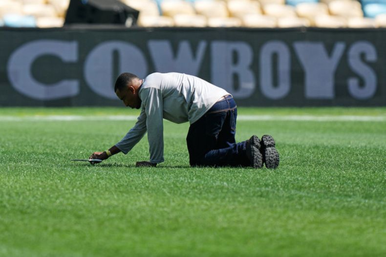 Un trabajador corta el césped con tijeras en el terreno de juego previo a un partido de fútbol americano de la NFL entre los Cowboys de Dallas y los Ravens de Baltimore en Río de Janeiro, el 26 de septiembre de 2026. (Foto AP/Fernando Llano)