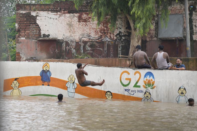 Residentes de las orillas del río Yamuna están sentados junto a una calle inundada en Nueva Delhi, India, jueves 13 de julio de 2023. Las inundaciones obligaron a evacuar a miles de personas en las zonas bajas de la capital. (AP Foto/Manish Swarup)