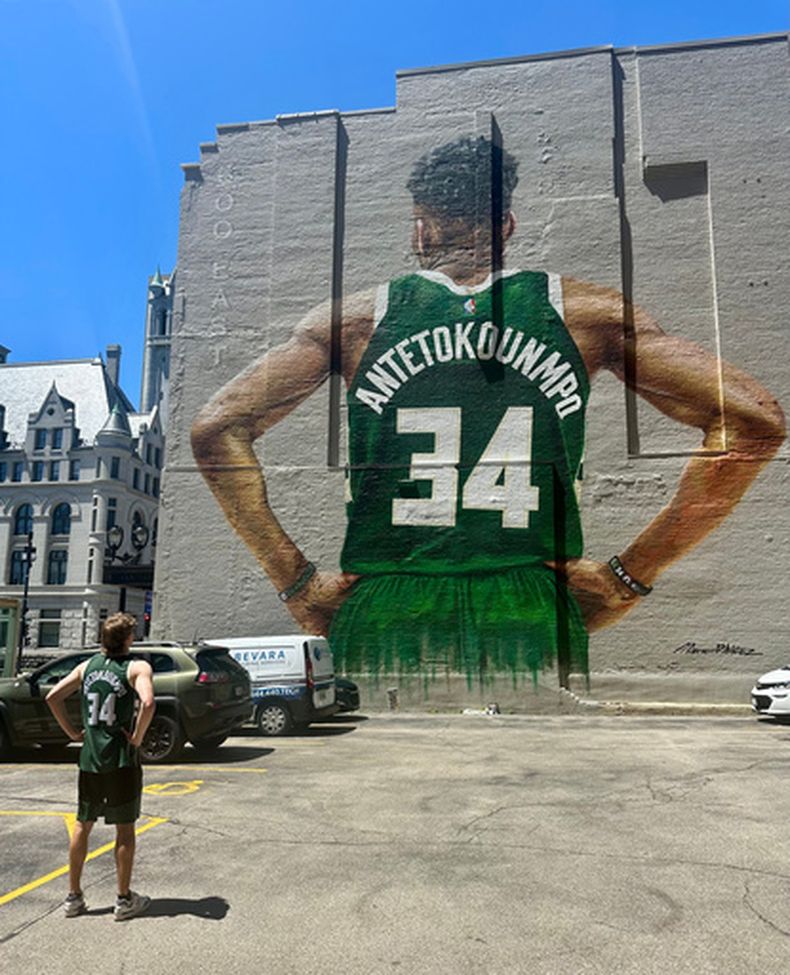 Danny Nelson luce una camiseta de los Bucks de Milwaukee de Giannis Antetokounmpo mientras contempla un mural suyo en el centro de Milwaukee el martes 23 de junio de 2026. (Foto AP/Steve Megargee)