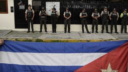 La gente ondea una bandera cubana mientras la policía hace guardia frente a la embajada de Cuba en Quito, Ecuador, el jueves 5 de marzo de 2026. (Foto AP/Carlos Noriega)