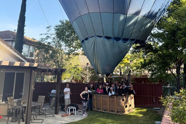 En esta fotografía cortesía de Hunter Perrin se puede ver a personas dentro de la canastilla de un globo aerostático posando para una fotografía después de un aterrizaje de emergencia en el jardín de Perrin, el sábado 18 de abril de 2026, en Temecula, California. (Hunter Perrin vía AP)