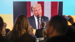 Varias personas siguen la toma de posesión de Donald Trump en pantallas en la casa de Ucrania, en el Foro Económico Mundial, en Davos, Suiza, el 20 de enero de 2025. (AP Foto/Markus Schreiber)