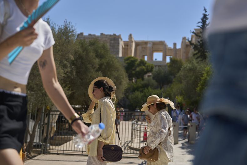 Turistas caminan fuera de la Acrópolis de Atenas, el lunes 7 de julio de 2025, mientras las autoridades en Grecia imponían paros obligatorios en el trabajo en zonas del país donde se esperaban más de 4 grados Celsius (104 Fahrenheit) (AP Foto/Petros Giannakouris)