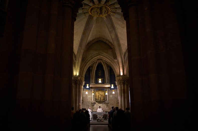Un sacerdote celebra una misa en la cripta de Antoni Gaudí bajo la Sagrada Familia mientras una multitud de visitantes llena la basílica en el piso superior, en Barcelona, España, el 15 de mayo de 2026. (AP Foto/Emilio Morenatti)
