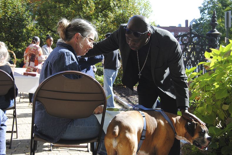 El reverendo Jean Beniste, un inmigrante haitiano, bendice a un perro y a su propietaria, el sábado 5 de octubre de 2024, durante el evento de Bendición de Animales en el jardín de la Iglesia Episcopal St. Paul de Concord, Nueva Hampshire. (G. Jeffrey MacDonald vía AP)