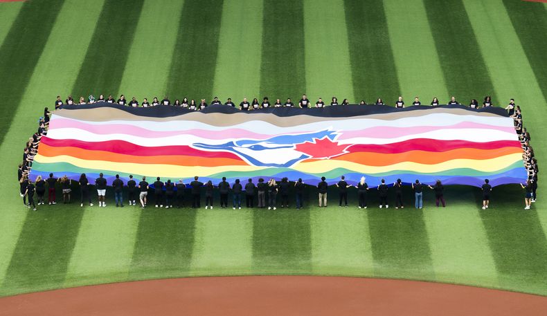 Un grupo de personas sostiene una bandera de los Azulejos de Toronto para festejar el Fin de Semana del Orgullo, antes del juego ante los Mellizos de Minnesota, el viernes 9 de junio de 2023 (Mark Blinch)