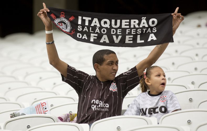 Un obrero muestra una pancarta con el mensaje "Itaquerao, el vest&iacute;bulo de la favela", mientras mira un partido de pr&aacute;ctica en la construcci&oacute;n del estadio de Sao Paulo para la Copa del Mundo el jueves, 1 de mayo de 2014, en S