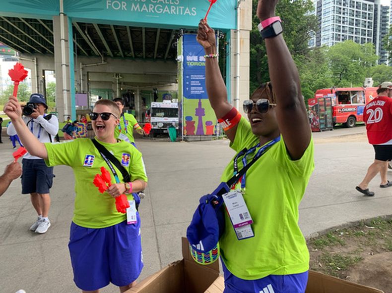 Las voluntarias Nicole Johnston (izquierda) y Mbalu Lumor (derecha) agitan aplaudidores canadienses (Canadian clappers) antes de repartirlos a los asistentes en el FIFA Fan Festival, el miércoles 24 de junio de 2026, en Toronto. (Foto AP/Mike Householder)