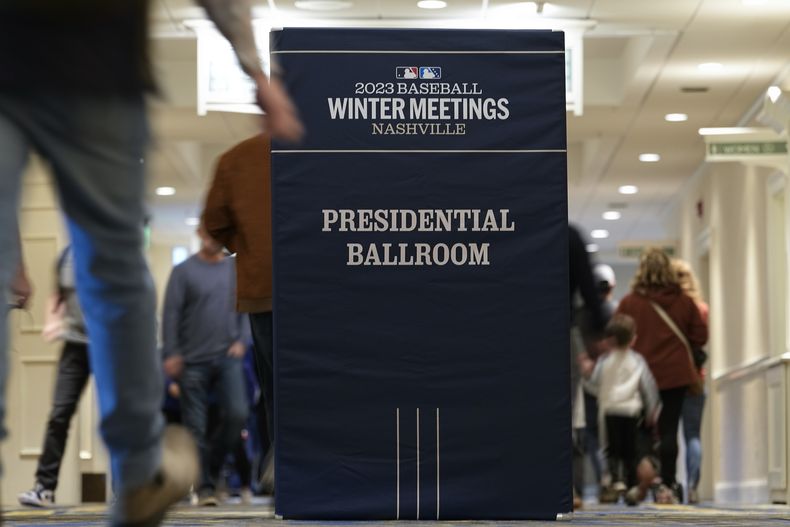 Personas pasan a un costado de un anuncio de las Reuniones de Invierno del Béisbol de las Grandes Ligas, el lunes 4 de diciembre de 2023, en Nashville, Tennessee. (AP Foto/George Walker IV)