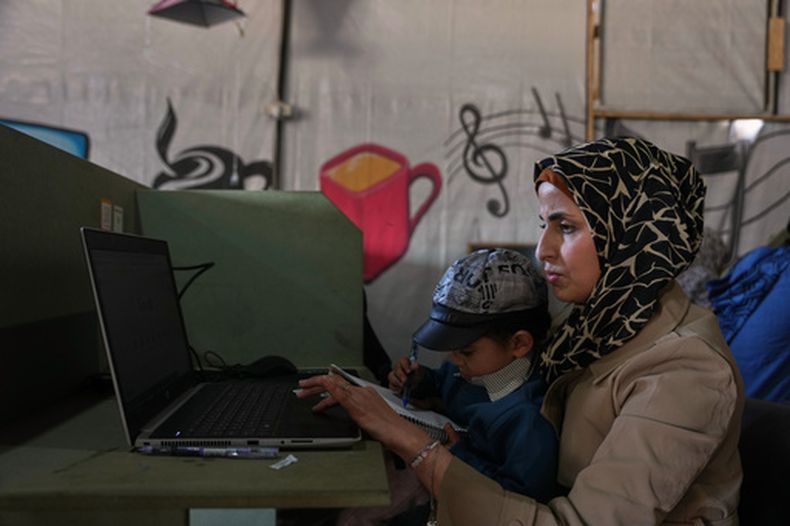 La diseñadora gráfica palestina Reem Alkhateeb, de 33 años, trabaja en su computadora junto a su hijo en un espacio de coworking en Jan Yunis, sur de la Franja de Gaza, el 9 de marzo de 2026. (Foto AP/Abdel Kareem Hana)