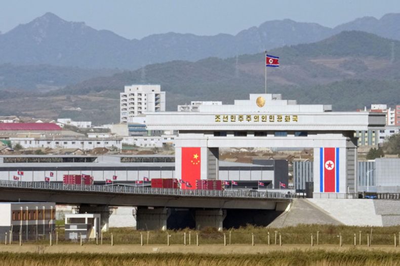 Las banderas de China y Corea del Norte pueden verse a los costados de una puerta de acceso a una instalación aduanera norcoreana —vista desde Dandong, China—, el miércoles 14 de octubre de 2026, antes de la ceremonia de inauguración del puente sobre el río Yalu, que conecta a ambos países. (Iori Sagisawa/Kyodo News vía AP)