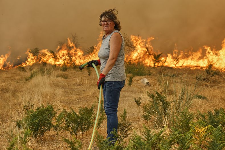 Una mujer con una manguera trata de apagar un incendio en Santa Baia De Montes, en el noroeste de España, el 14 de agosto de 2025. (AP Foto/Lalo R. Villar)