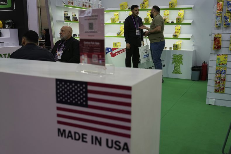 Un trabajador platica con un visitante en el puesto de Exotica Freshener Co, una compañía estadounidense que vende aromatizantes, en la 137ma Feria de Cantón en Guangzhou, en la provincia china de Guangdong, el martes 15 de abril de 2025. (AP Foto/Ng Han Guan)