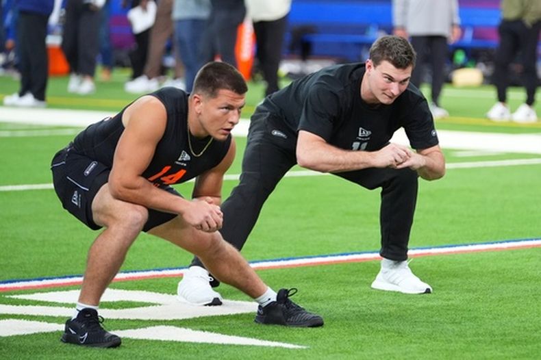 Diego Pavia (14), quarterback de Venderbilt, y Fernando Mendoza (11), quarterback de Indiana, estiran los músculos en el Scouting Combine de la NFL el sábado 28 de febrero de 2026, en Indianápolis. (AP Foto/Julio Cortez)