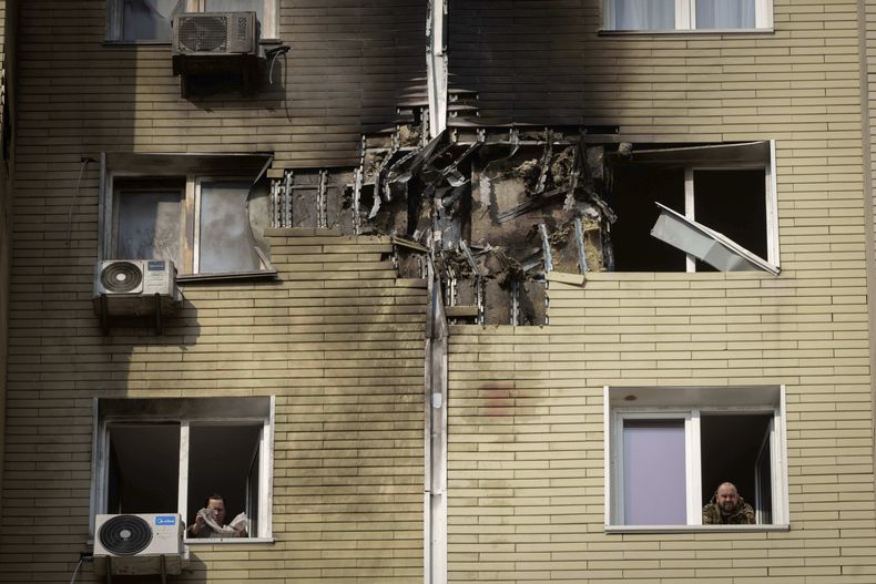 Un hombre mira mientras su vecina limpia un apartamento dañado en un edificio de viviendas de varias plantas tras un ataque de don ruso durante la noche en Kiev, Ucrania, el domingo 23 de marzo de 2025. (AP Foto/Efrem Lukatsky)