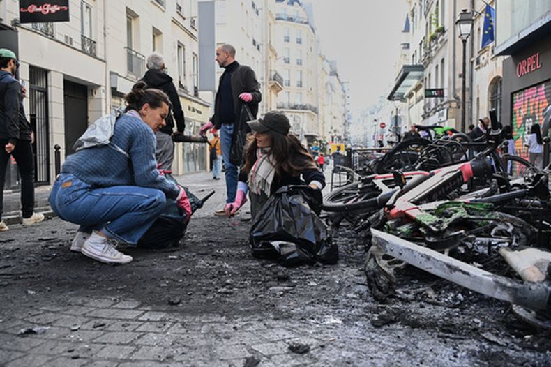 Varias personas recogen escombros en una calle, junto a bicicletas quemadas, un día después de una manifestación contra el aumento en el costo de vida y en solidaridad con las quejas de los estudiantes, en París, el domingo 18 de octubre de 2026. (AP Foto/Emma Da Silva)