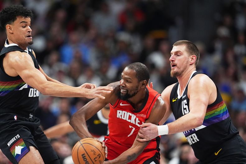El alero de los Rockets de Houston, Kevin Durant, al centro, busca pasar el balón mientras el alero de los Nuggets de Denver, Spencer Jones, y el pívot Nikola Jokić defienden en la primera mitad de un juego de baloncesto de la NBA el sábado 20 de diciembre de 2025, en Denver. (AP Photo/David Zalubowski)