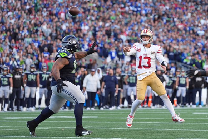 El quarterback de los 49ers de San Francisco, Brock Purdy (13), lanza un pase de conversión de dos puntos mientras el tackle defensivo de los Seahawks de Seattle, Byron Murphy II (91), intenta ejercer presión durante la segunda mitad de un partido de fútbol americano de la NFL, el domingo 11 de octubre de 2026, en Seattle. (Foto AP/Lindsey Wasson)