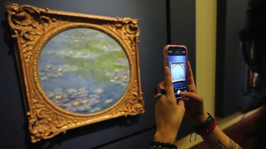 Un visitante toma fotografías de una pintura de Claude Monet durante una gira de prensa de la exposición: La Revolución Impresionista, en el Palacio de Bellas Artes en la Ciudad de México, el lunes 24 de marzo de 2025. (Foto AP/Fernando Llano)