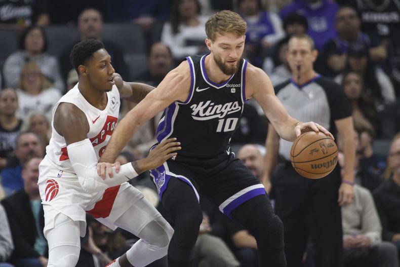 Domantas Sabonis, alero lituano de los Kings de Sacramento, avanza con el balón delante de RJ Barrett, de los Raptors de Toronto, el viernes 5 de enero de 2024 (AP Foto/Randall Benton)