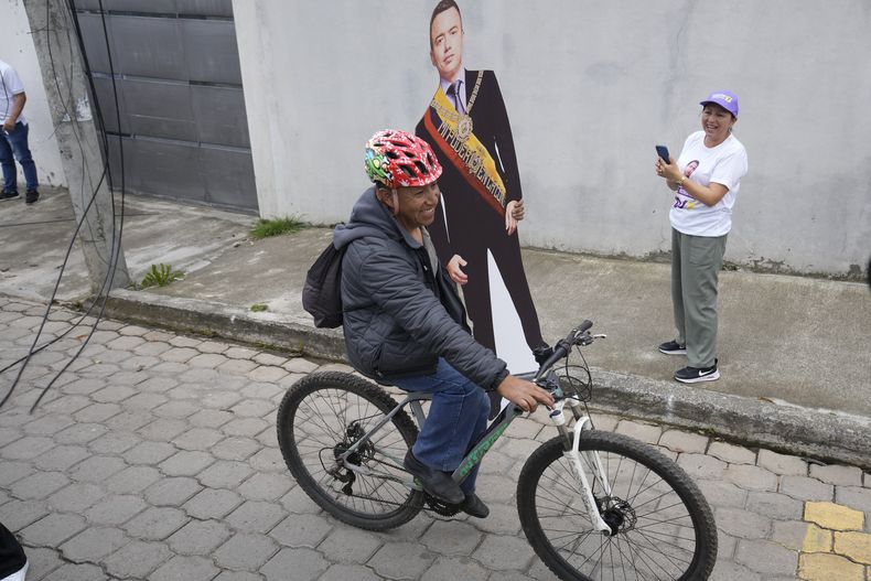 Un simpatizante pasa en bicicleta con una figura de tamaño natural del presidente Daniel Noboa, que se postula para la reelección, mientras los residentes esperan su llegada a un acto de campaña antes de las próximas elecciones generales del 9 de febrero, en Cayambe, Ecuador, el sábado 18 de enero de 2025. (Foto AP/Dolores Ochoa)