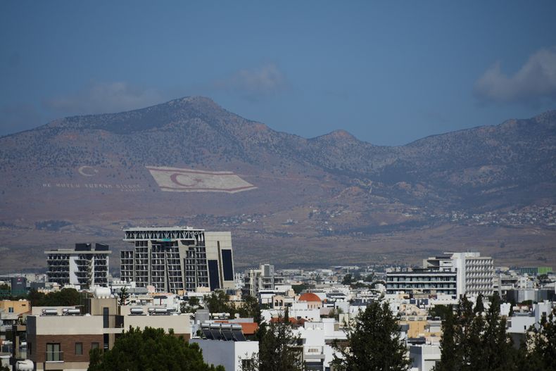 Vista de edificaciones en Nicosia, la capital dividida de Chipre, con una gigantesca bandera turca en el fondo, derecha, y la medialuna turca, izquierda, en la montaña Pentadahtilos, en la zona ocupada por Turquía, en la parte norte de la isla, el viernes 24 de octubre de 2025. (AP Photo/Petros Karadjias)