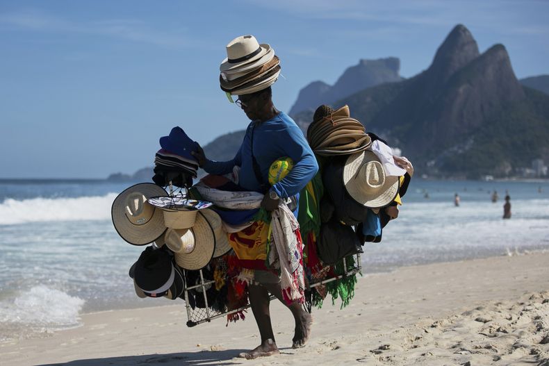 Un vendedor camina con sombreros y ropa en la playa de Ipanema, en Río de Janeiro, el domingo 25 de mayo de 2025. (AP Foto/Bruna Prado)