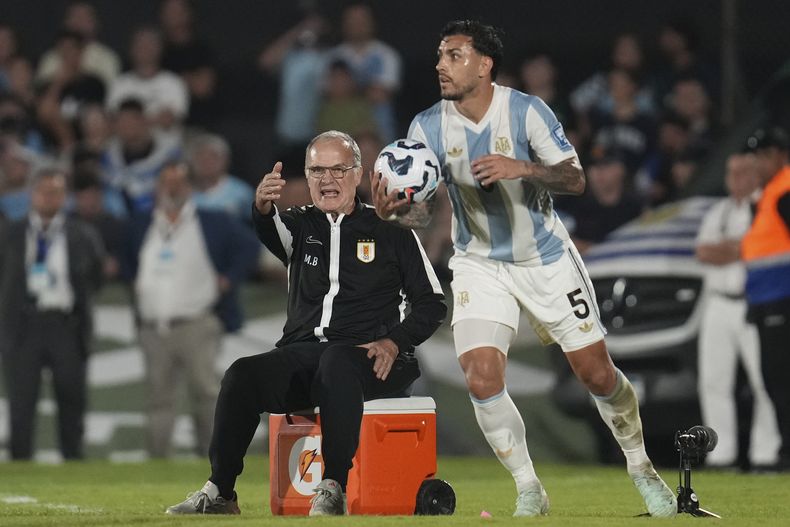 El técnico de Uruguay Marcelo Bielsa, sentado en un hielera, da instrucciones frente al volante argentino Leandro Paredes sostiene la pelota durante el partido de las eliminatorias del Mundial, el viernes 21 de marzo de 2025, en Montevideo. (AP Foto/Matilde Campodónico)