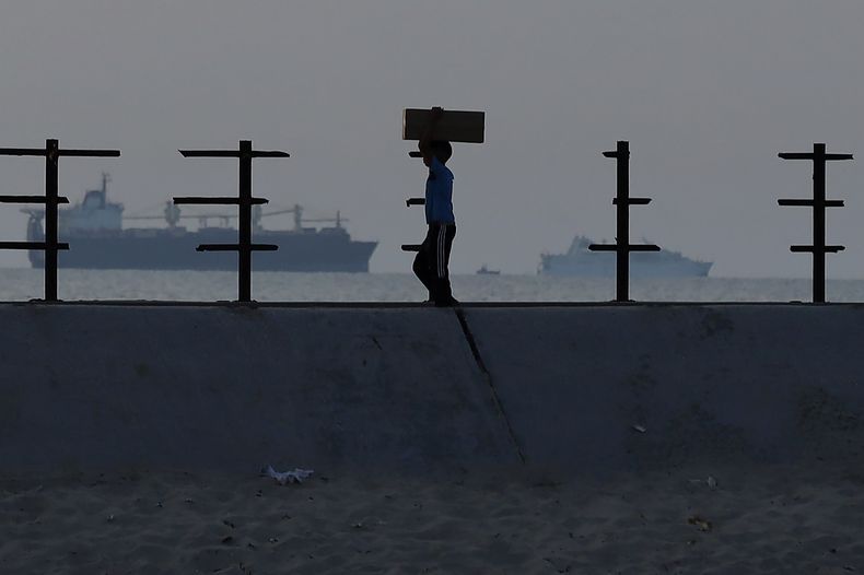 Un niño palestino lleva una caja de ayuda en la carretera de la playa del campamento de refugiados de Nusseirat, en el centro de la Franja de Gaza, el sábado 18 de mayo de 2024, luego de que la gente se abalanzara sobre camiones cargados de ayuda humanitaria introducida a través de un nuevo muelle construido por Estados Unidos. (AP Foto/Saher Alghorra)