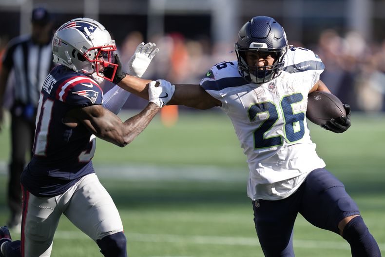 El running back de los Seahawks de Seattle Zach Charbonnet (26) corre con el balón mientras el cornerback de los Patriots de Nueva Inglaterra Jonathan Jones (31) defiende en el tiempo extra, el domingo 15 de septiembre de 2024, en Foxborough, Massachusetts (AP Foto/Charles Krupa)