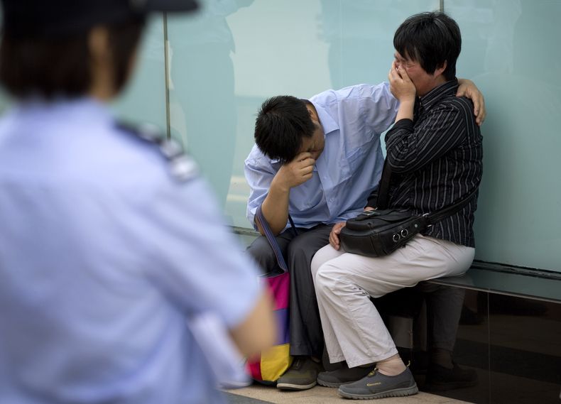 Una polic&iacute;a observa a una pareja llorar porque representantes de la aerol&iacute;nea Malaysia Airlines se negaron a recibirlos en las oficinas de la empresa en Beijing, China, el mi&eacute;rcoles 11 de junio de 2014. El hijo de la pareja era una de