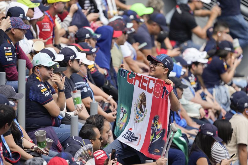 Un fanático del piloto mexicano Sergio Pérez posa para fotos con una bandera mexicana durante la tercera práctica libre previo al Gran Premio de México, en el Autódromo Hermanos Rodríguez, en la Ciudad de México, el sábado 26 de octubre de 2024. (AP Foto/Eduardo Verdugo)