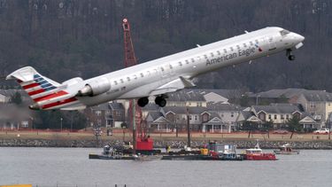 Mientras un avión de American Eagle despega, cuadrillas realizan tareas de recuperación cerca del punto en el río Potomac donde cayeron los restos de un avión comercial y un helicóptero militar que chocaron en pleno vuelo en el Aeropuerto Nacional Ronald Reagan, el jueves 6 de febrero de 2025, en Arlington, Virginia. (AP Foto/José Luis Magaña)