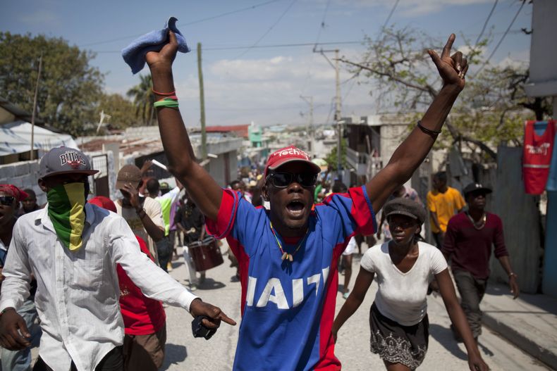 Manifestantes corean consignas contra el gobierno durante una protesta para recordar el d&eacute;cimo aniversario del segundo derrocamiento del expresidente Jean-Bertrand Aristide, en Puerto Pr&iacute;ncipe, Hait&iacute;, el jueves 27 de febrero de 2014.