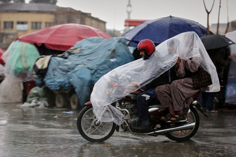 Un hombre conduce una motocicleta con dos pasajeros bajo una cubierta de plástico bajo una fuerte lluvia en Kabul, Afganistán, el 31 de marzo de 2026. (Foto AP/Siddiqullah Alizai)