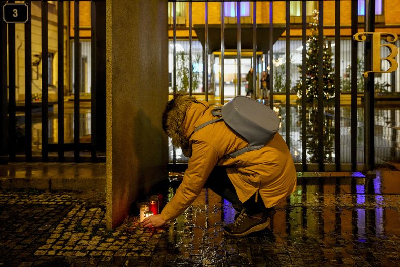 Una mujer enciende velas afuera del edificio de la Facultad de Filosofía de la Universidad Charles en el centro de Praga, República Checa, el jueves 21 de diciembre de 2023. (AP Foto/Petr David Josek)