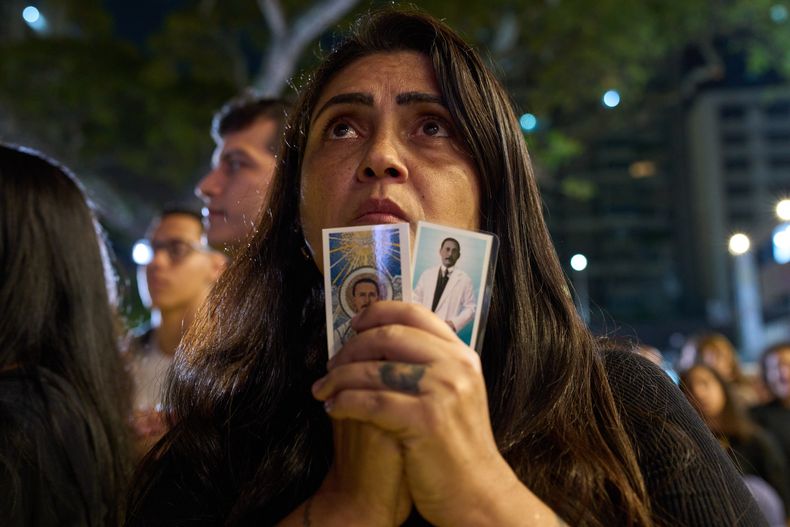Una católica sostiene imágenes de José Gregorio Hernández durante un evento para celebrar la canonización del primer santo venezolano, Hernández, por parte del papa León XIV, en una plaza de Caracas, Venezuela, el domingo 19 de octubre de 2025. (AP Foto/Ariana Cubillos)