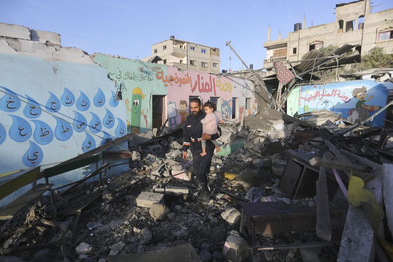 Palestinos pasan junto a un edificio destruido por un bombardeo nocturno israelí, en Rafah, en la Franja de Gaza, el 24 de noviembre de 2023. (AP Foto/Hatem Ali)