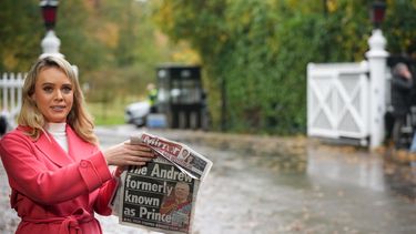 Una presentadora de televisión sostiene un periódico con una foto del príncipe Andrés mientras habla a la cámara en una puerta cerca del Royal Lodge, tras el anuncio de que a Andrés se le retirarán sus títulos nobiliarios y abandonará la mansión de 30 habitaciones que ha ocupado durante más de 20 años en Windsor, Inglaterra, el viernes 31 de octubre de 2025. (Foto AP/Alastair Grant)