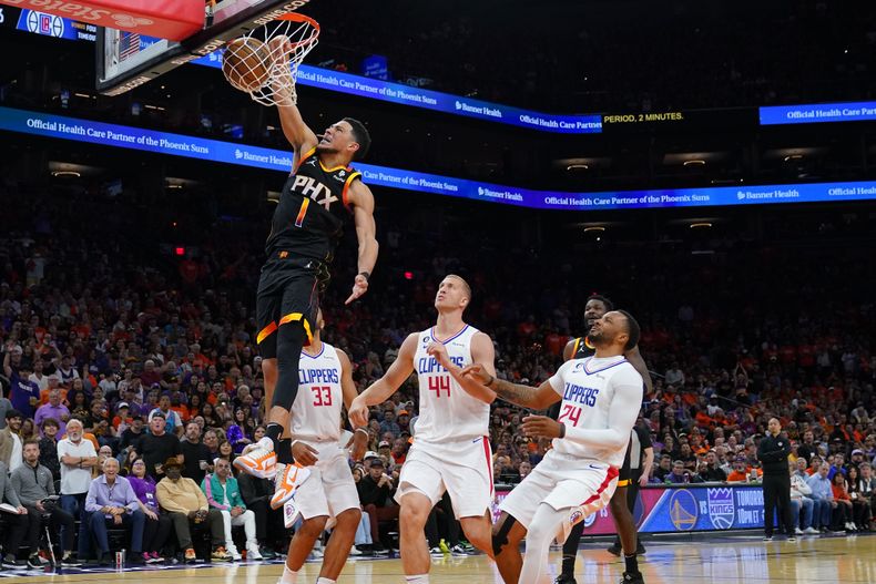 Devin Booker (1), de los Suns de Phoenix, anota un mate frente a sus rivales de los Clippers de Los Ángeles Mason Plumlee (44), Nicolas Batum (33) y Norman Powell (24) durante la segunda mitad del quinto juego de la primera ronda de los playoffs de la NBA, el 25 de abril de 2023, en Phoenix. (AP Foto/Matt York)