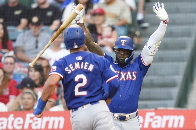 El cubano de los Rangers de Texas, Adolis García (derecha) reacciona mientras Marcus Semien (2) anota en un elevado de sacrificio por parte de Wyatt Langford durante el tercer episodio del juego de béisbol ante los Angelinos de Los Ángeles, el martes 9 de julio de 2024, en Anaheim. (AP Foto/Ryan Sun)