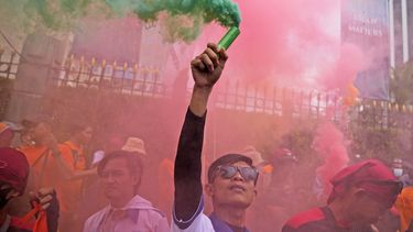 UN trabajador sostiene una bengala durante una manifestación del Primero de Mayo en Yakarta, Indonesia, el lunes 1 de mayo de 2023. Trabajadores y activistas en Asia reclamaban salarios más altos y mejores condiciones de trabajo, entre otras demandas. (AP Foto/Dita Alangkara)