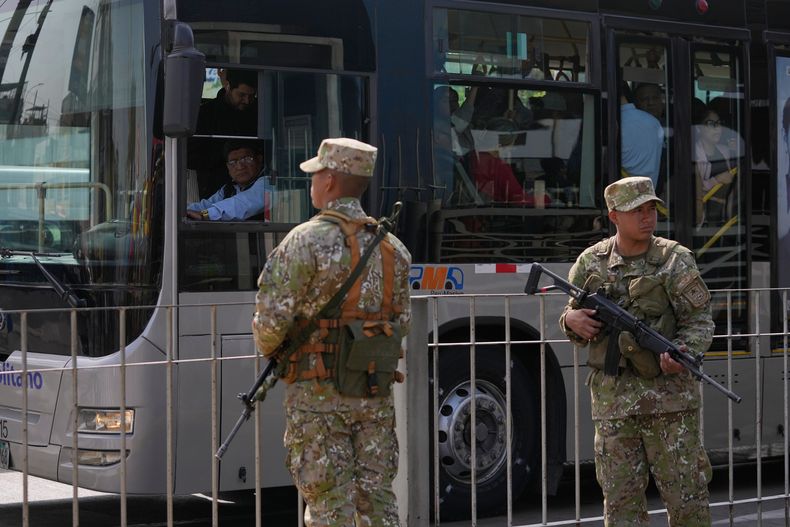 Un conductor de autobús observa a dos soldados que montan guardia en una parada de autobús en Lima, Perú, el miércoles 22 de octubre de 2025, después de que el presidente José Jerí declarara el estado de emergencia debido a la inseguridad. (AP Foto/Martín Mejía)