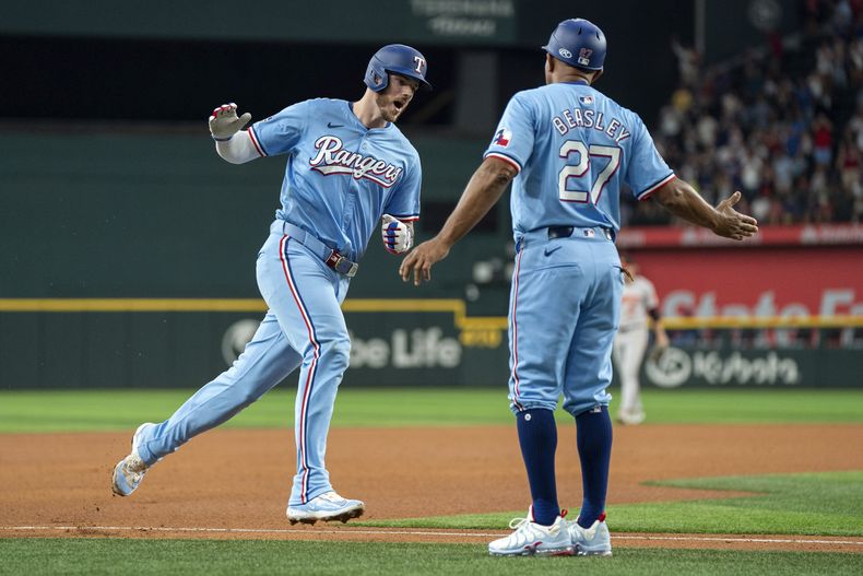 Jonah Heim, izquierda, de los Rangers de Texas, es felicitado por el coach de tercera base Tony Beasley (27) mientras se enfila al plato con su cuadrangular de tres carreras en el que también anotaron Wyatt Langford y Nathaniel Lowe durante la cuarta entrada del juego de béisbol en contra de los Orioles de Baltimore, el domingo 21 de julio de 2024, en Arlington, Texas. (AP Foto/Jeffrey McWhorter)