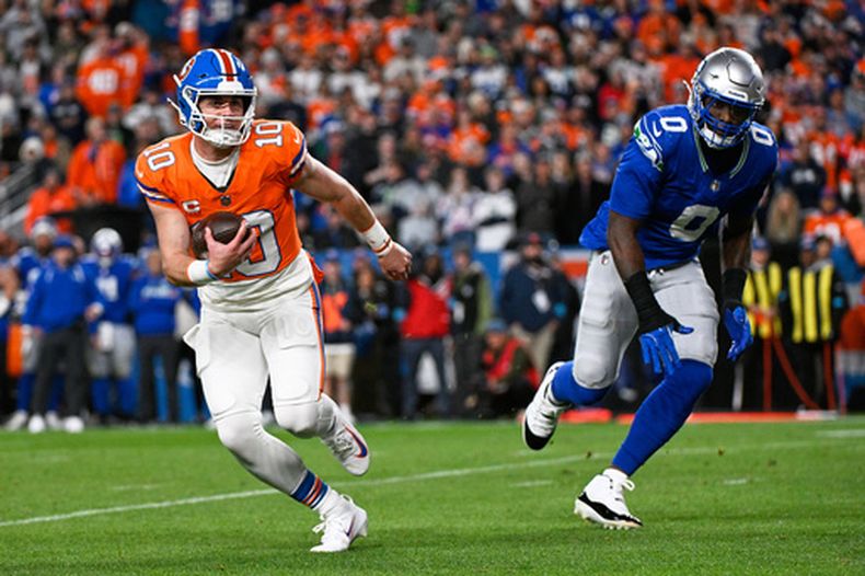 Bo Nix (10), quarterback de los Broncos de Denver, corre con el balón escapando de DeMarcus Lawrence (0), de los Seahawks de Seattle, durante la primera mitad del partido de la NFL, el jueves 15 de octubre de 2026, en Denver. (AP Foto/Geneva Heffernan)
