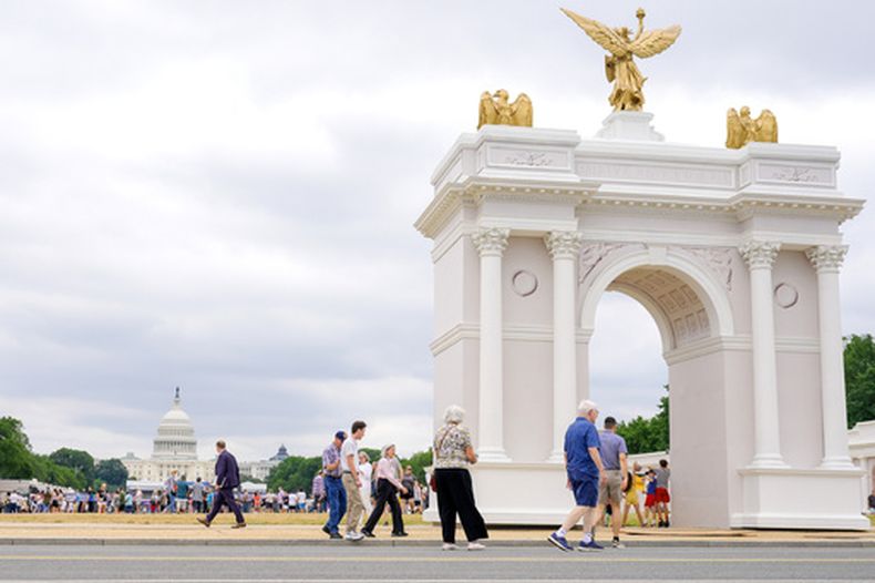 Varios visitantes caminan en la Gran Feria Estatal de Estados Unidos, con el modelo del arco del Triunfo y el Capitolio en el fondo, el miércoles 8 de julio de 2026, en Washington. (AP Foto/Mariam Zuhaib)